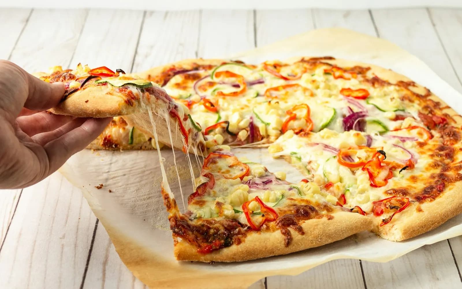 A slice of veg pizza being lifted, cheese stretching